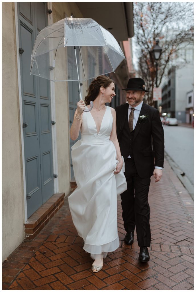 bride, carrying a clear umbrella, and groom wald the streets of New Orleans in the rain