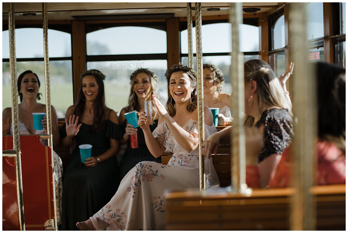 New Orleans bride and her bridesmaids travel via private streetcar to their photo destination, all laughing and sipping on cocktails.
