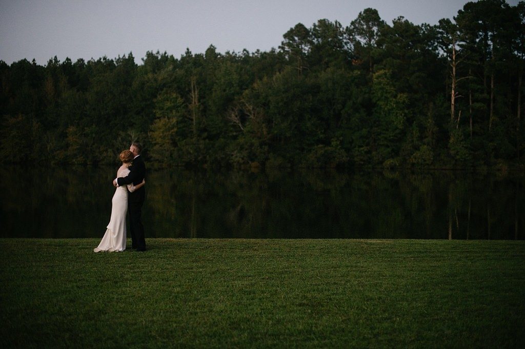 a bride and groom share a First Look beside a lake in a beautiful forest, smiling as they see each other for the first time.