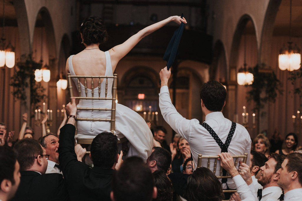 bride and groom are hoisted in the air on chairs for a traditional jewish wedding reception