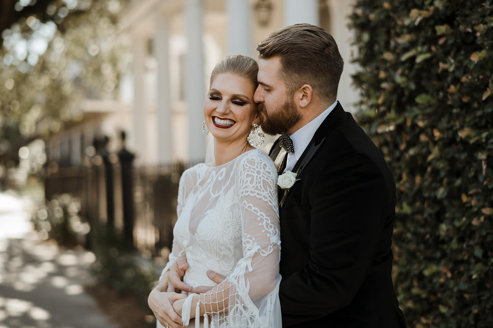 a bearded groom wearing a tux holds his gorgeous blond bride around the waist as she closes her eyes and smiles