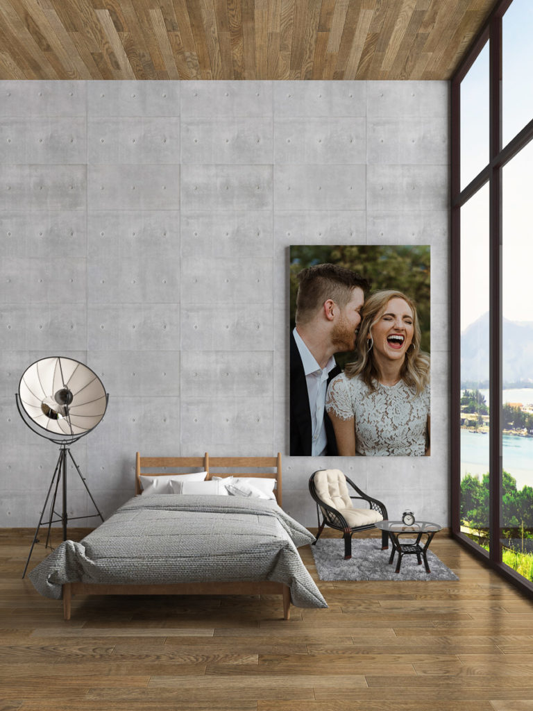 Giant canvas print of a man whispering in his fiancee's ear as she laughs big and loudly hanging on a bedroom wall